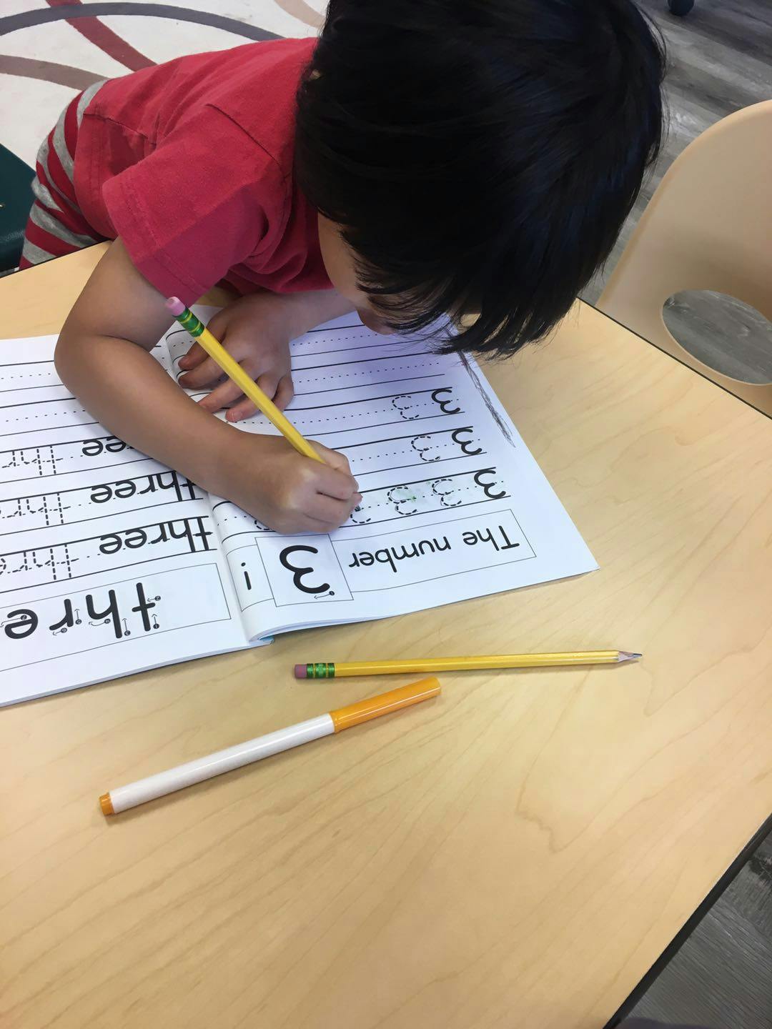 Child writing the number 3 in a workbook with a pencil