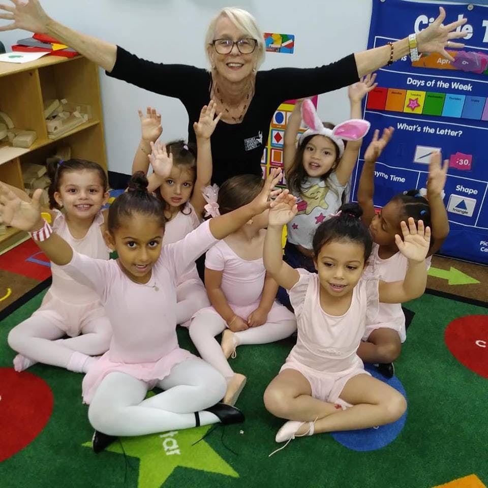 Adult and children in a classroom with arms raised