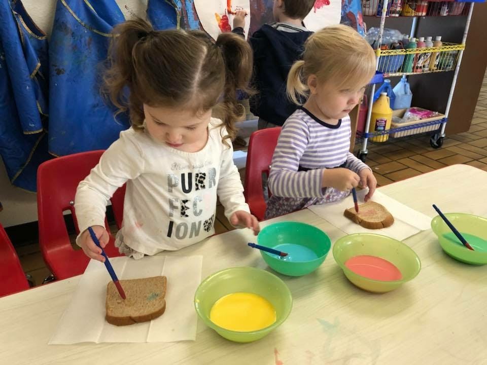 Two children painting on slices of bread at a table