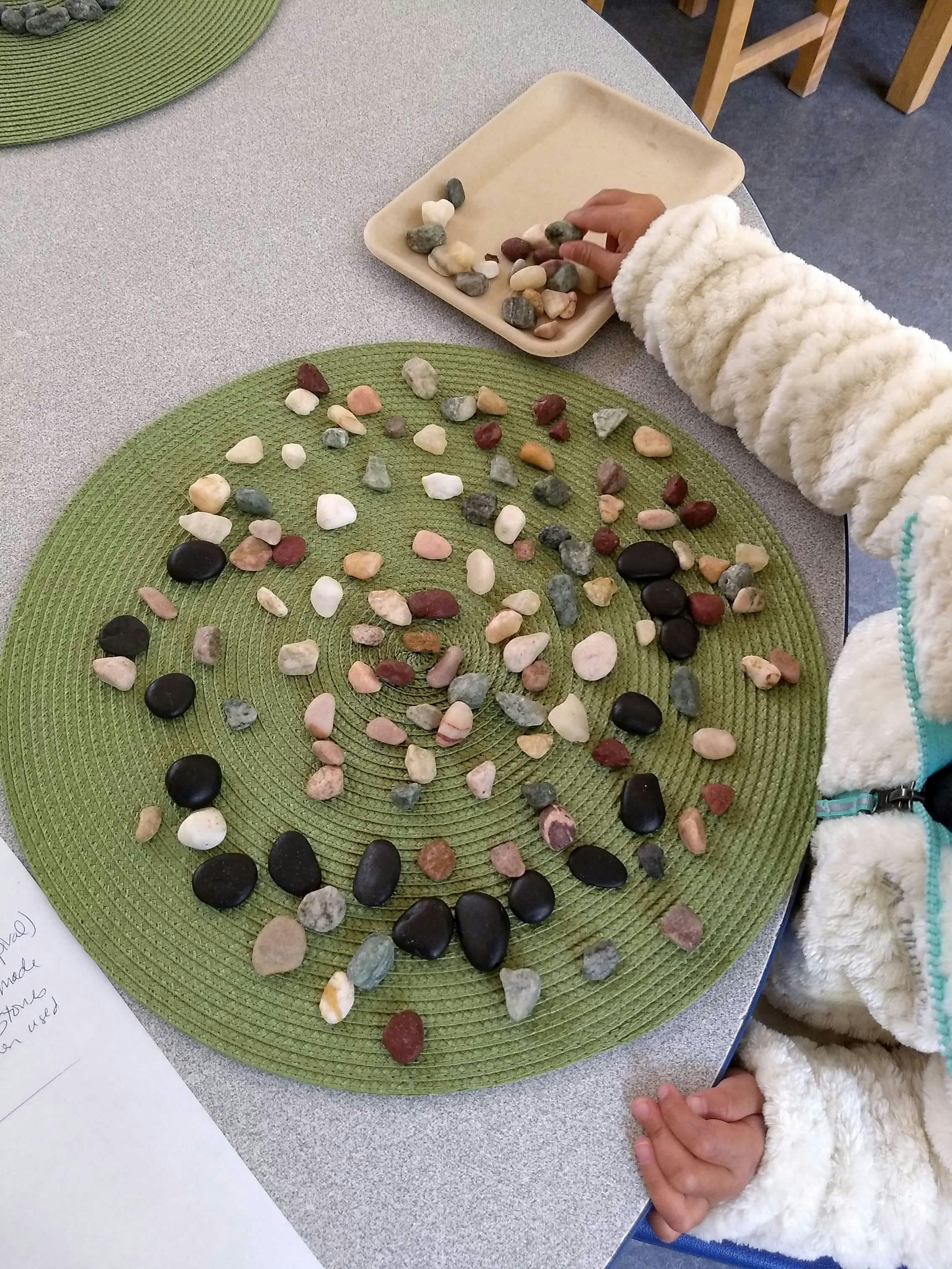 Child's hand pouring small rocks from a tray onto a green mat