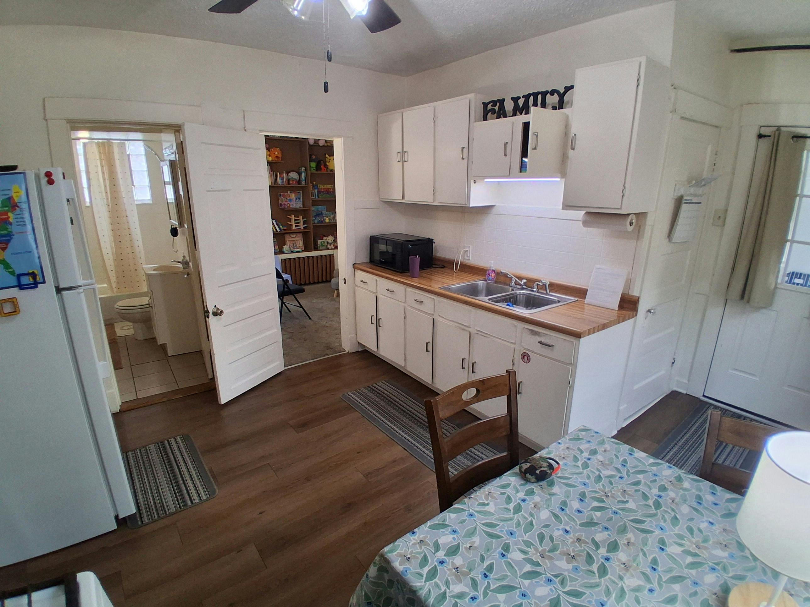 kitchen with white cabinets, a sink, microwave, and a table with a floral tablecloth