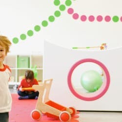 Child standing, another child playing with a tablet in a playroom