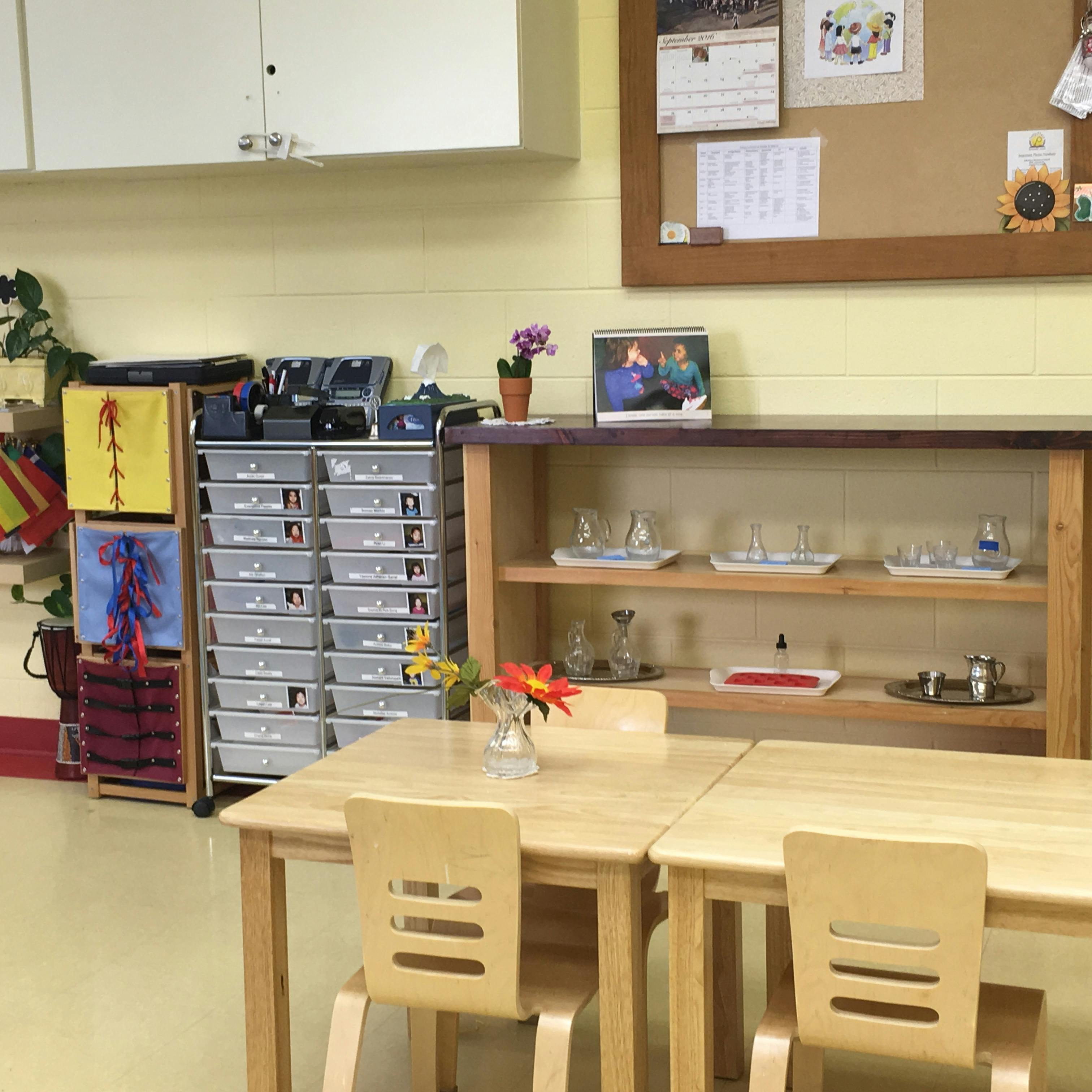 Classroom with small wooden tables and chairs, storage units, and shelves
