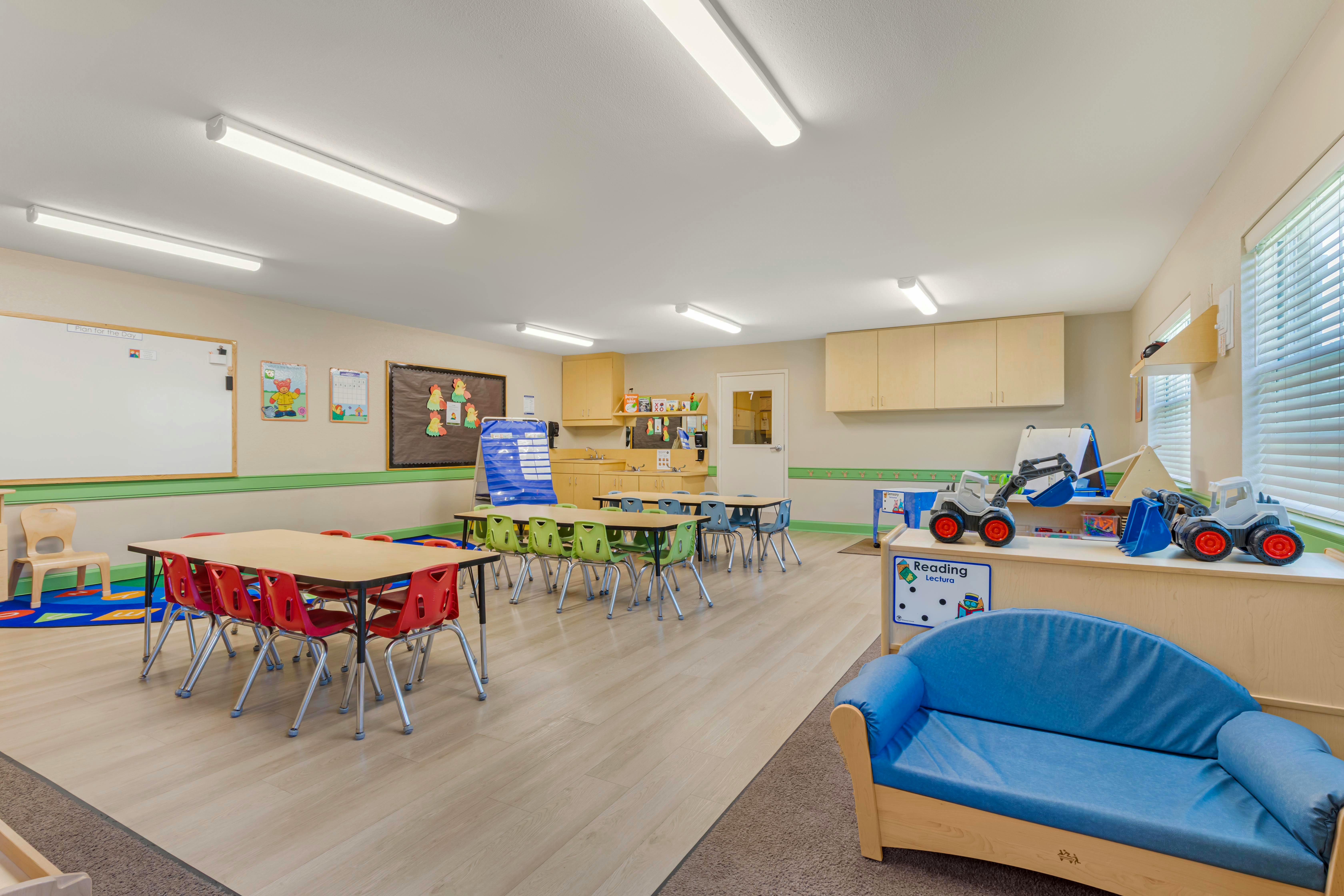Classroom with child-sized tables and chairs, a blue couch, and toy construction vehicles