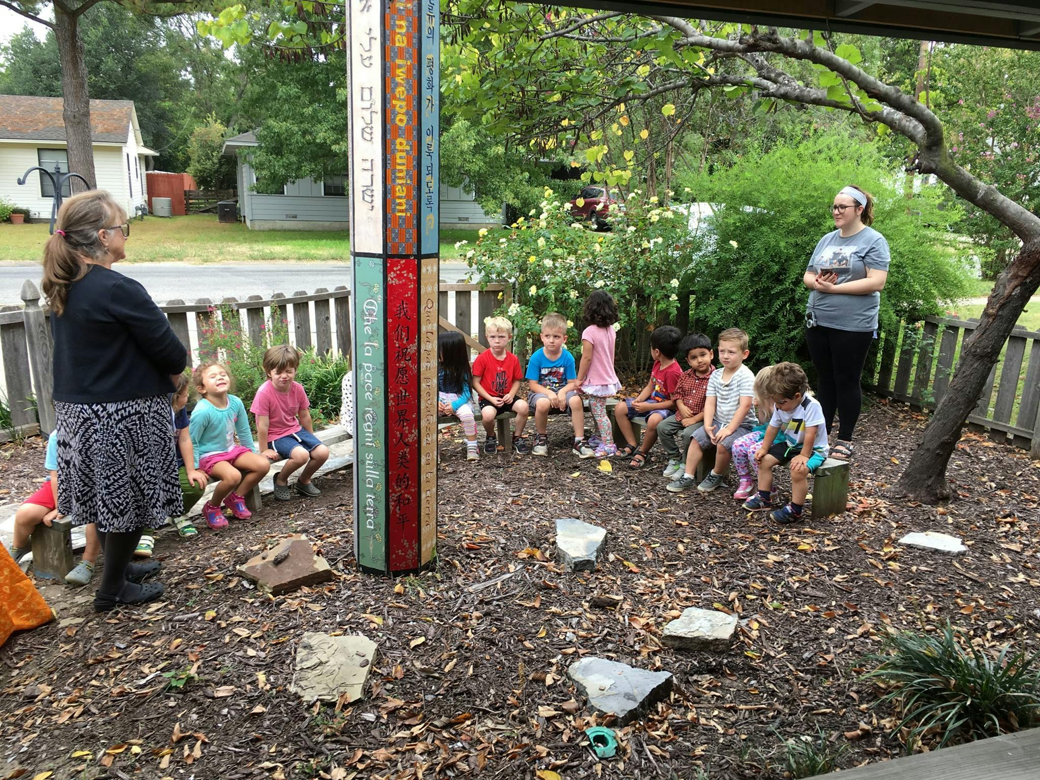 Two people standing with a group of children sitting on a bench outdoors