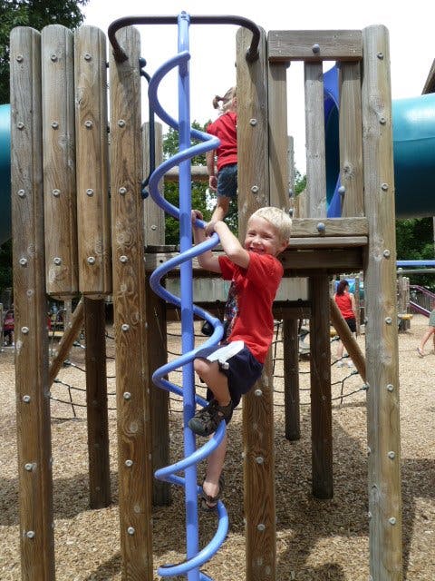 Child climbing a blue spiral ladder on a playground structure