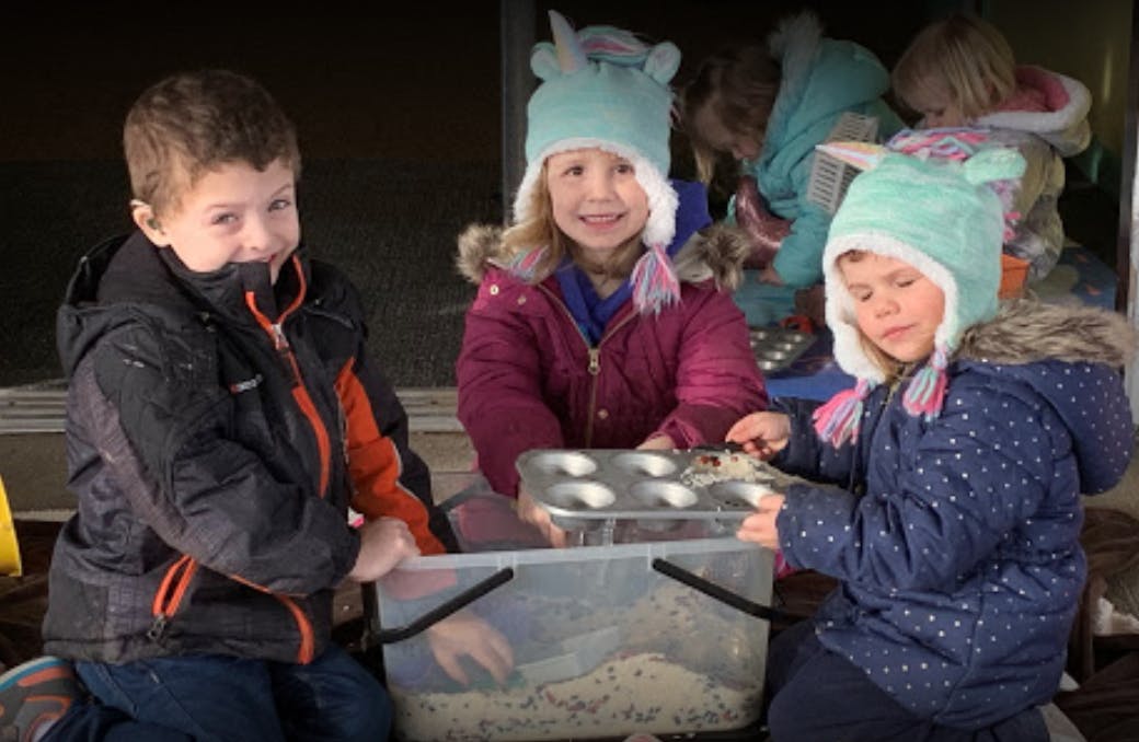 Three children playing with a container and a muffin tin