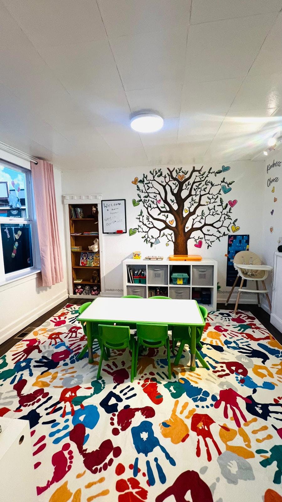 Classroom with a tree mural, small table and chairs, and handprint rug