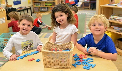 Three children playing with letter magnets at a table in a classroom