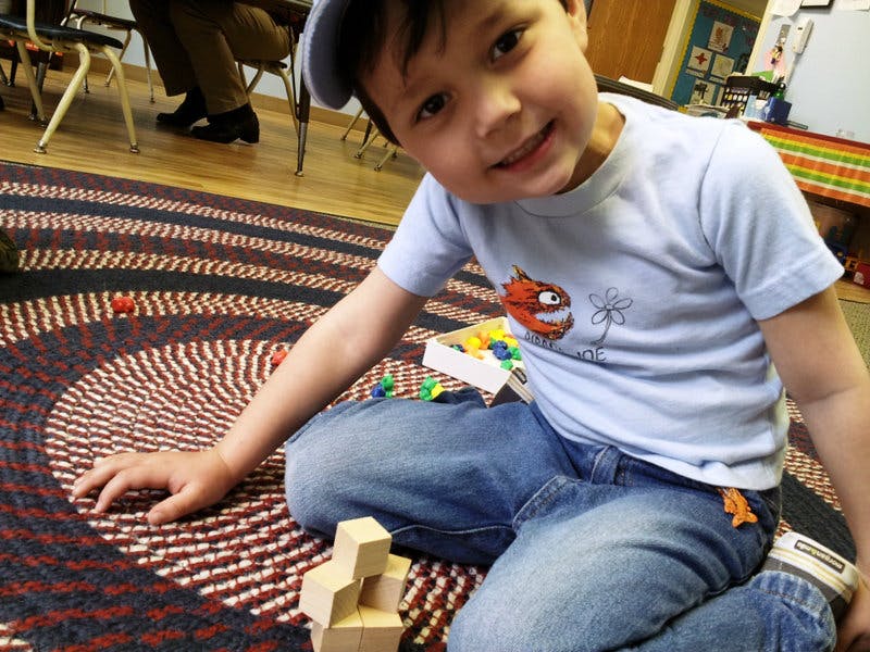 Child sitting on a rug with building blocks and small game pieces
