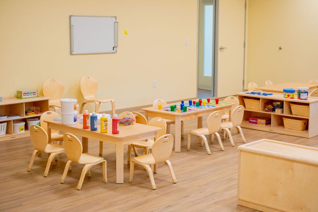Classroom with small wooden tables and chairs, art supplies, and board games