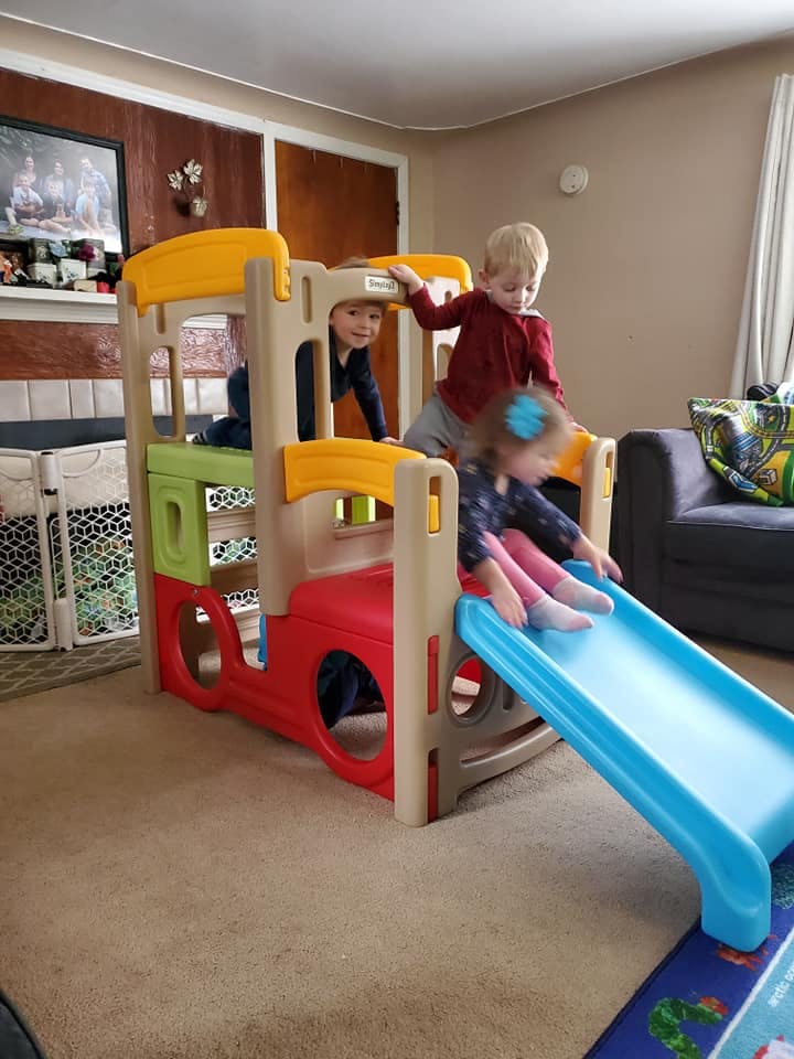 Three children playing on an indoor play structure with a slide