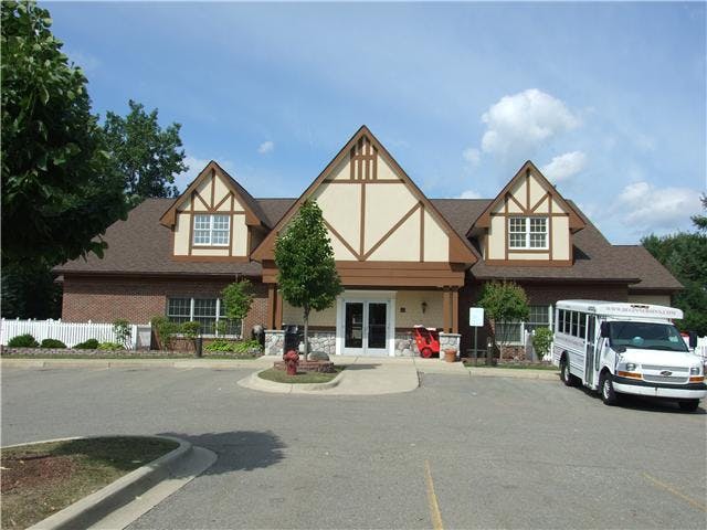 Building with Tudor-style gables and a white shuttle bus in a parking lot