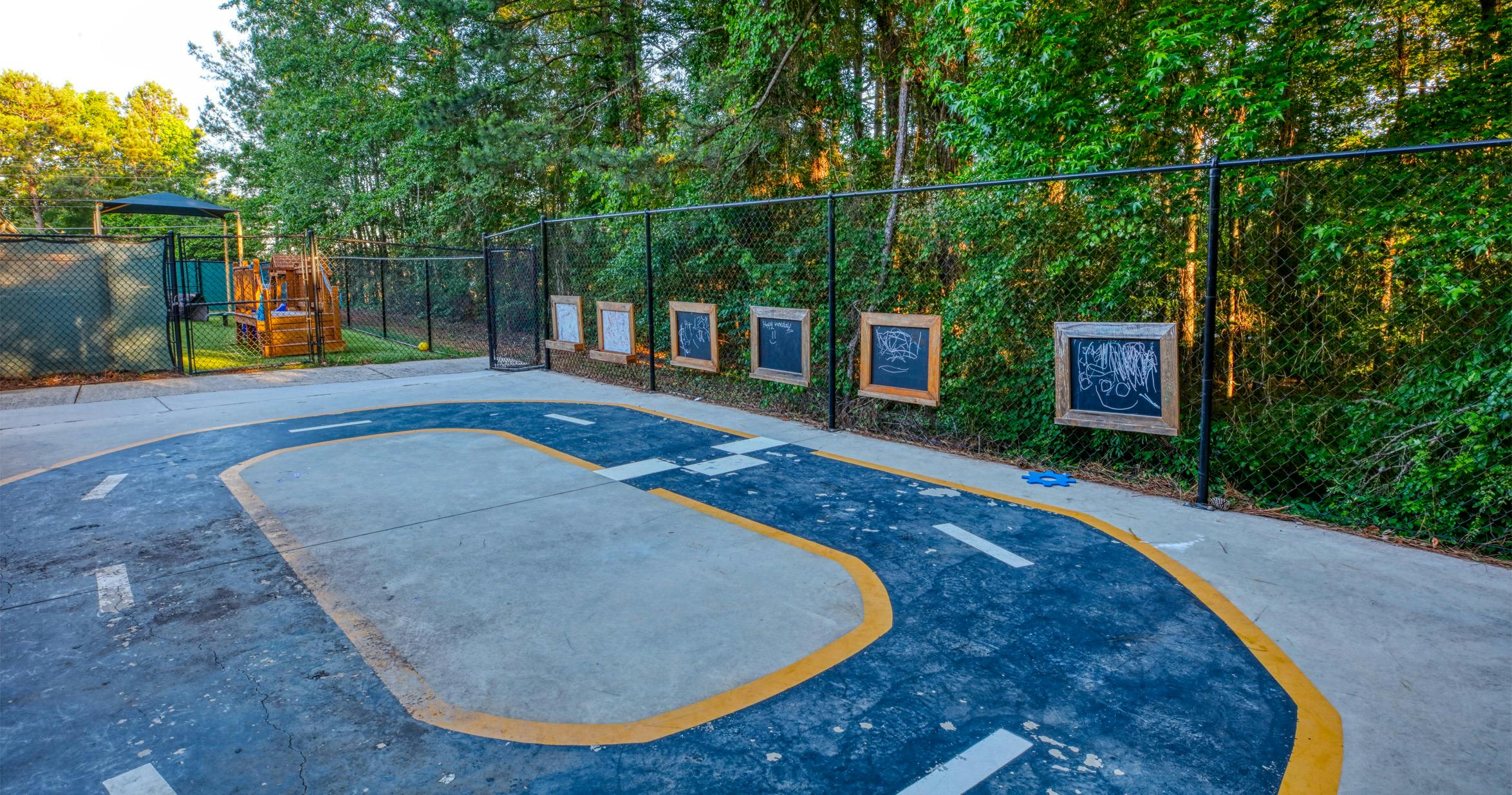 Outdoor play area with a painted road on concrete and chalkboards on a fence