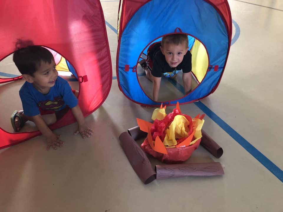 Two children crawling out of play tunnels toward a pretend campfire