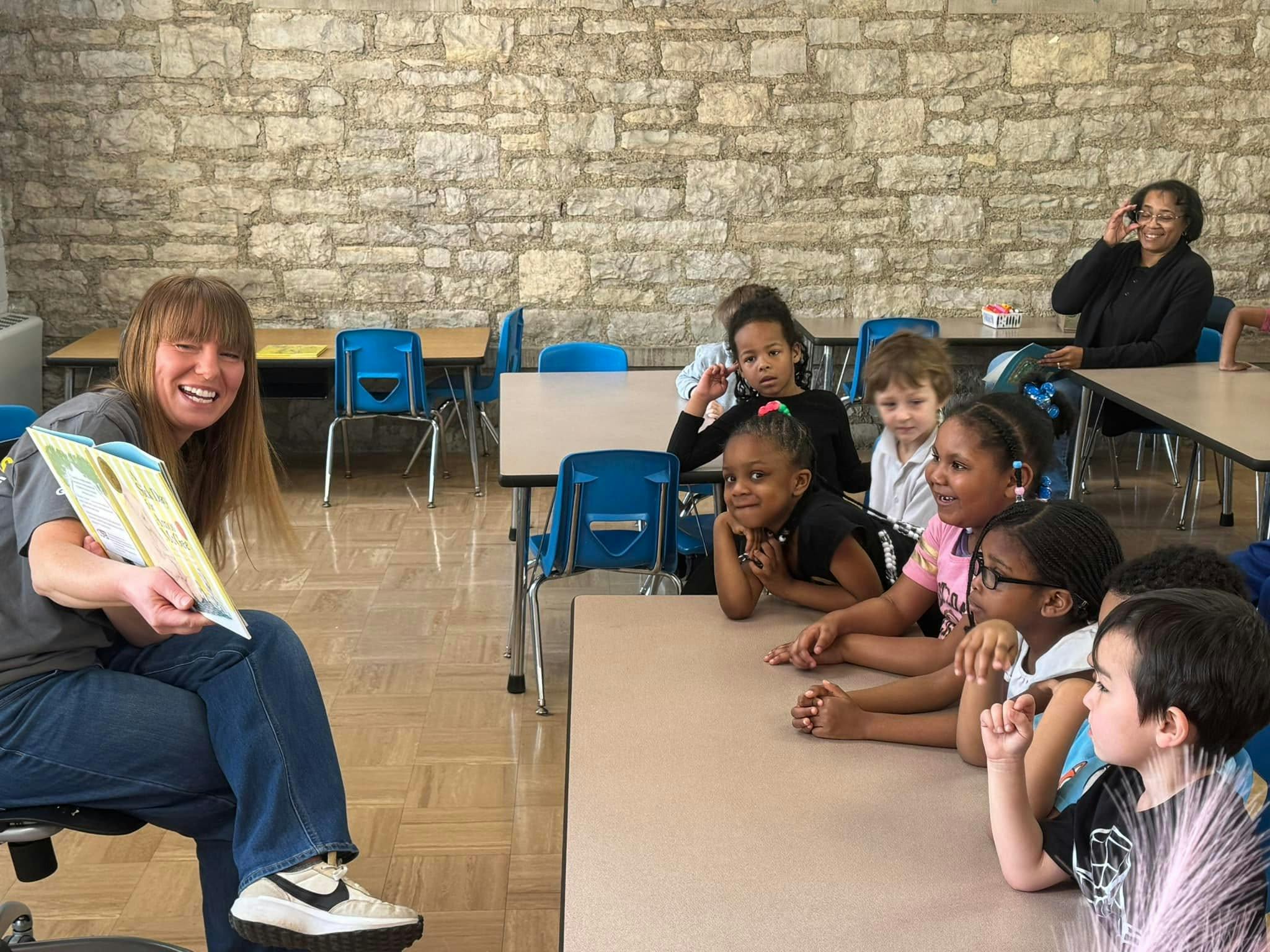 A person reading a book to a group of children in a classroom