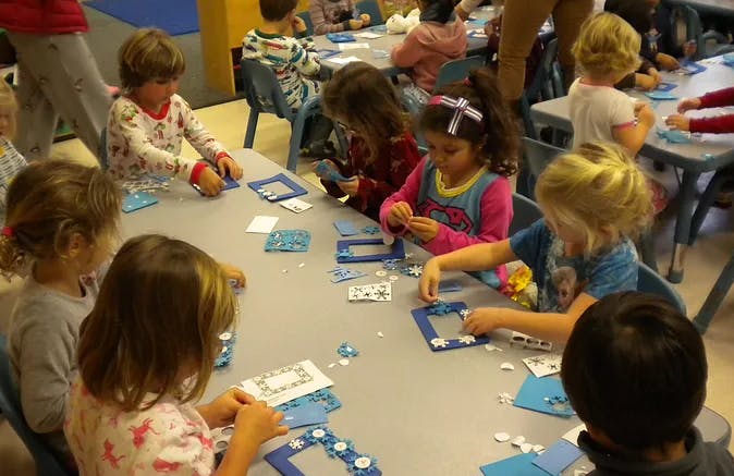 Children at tables doing crafts with crafts with blue paper and small white objects