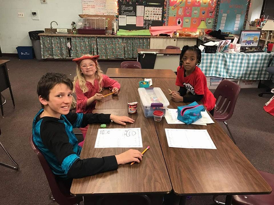 Three children sitting at desks in a classroom