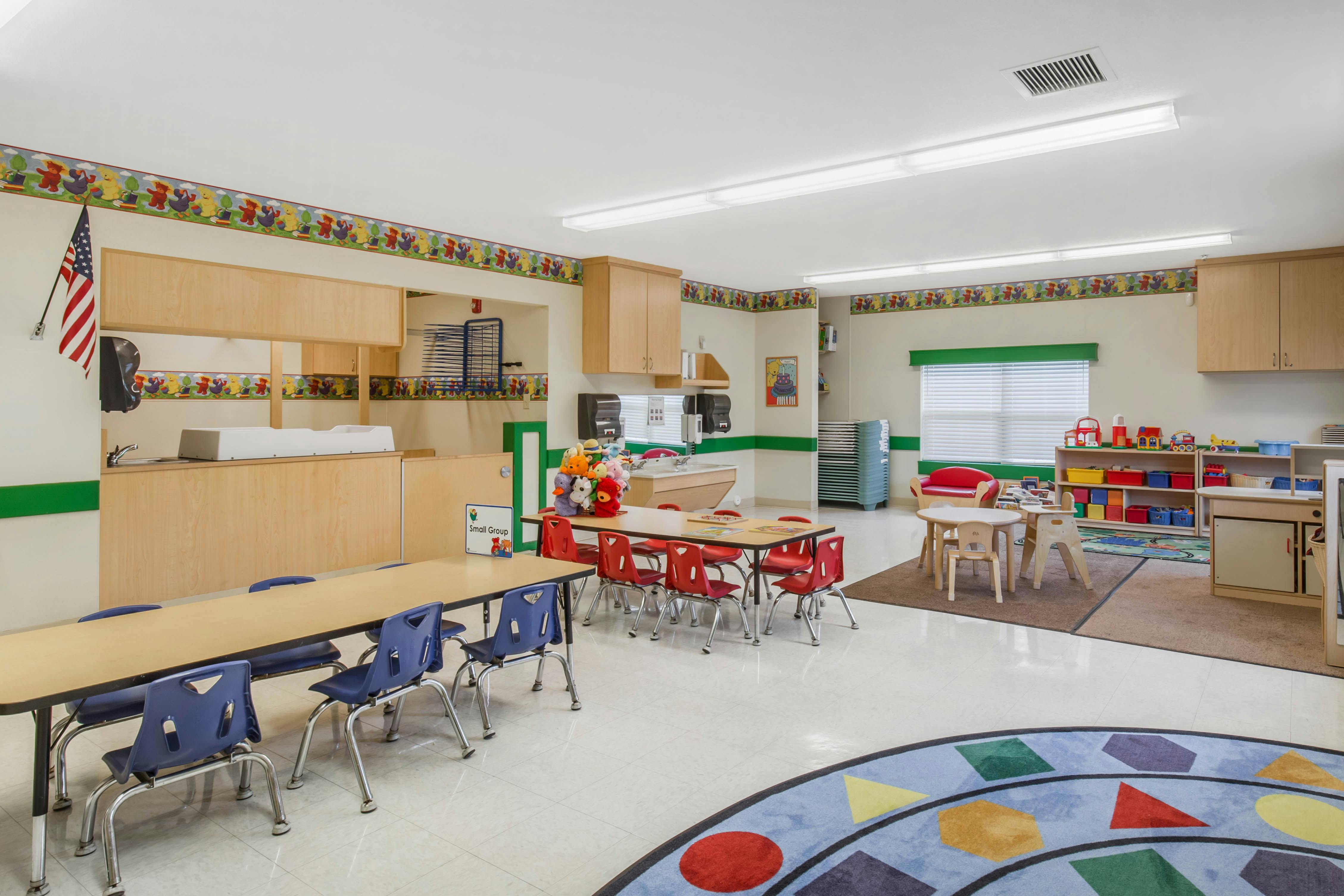 Classroom with child-sized tables and chairs, a changing station, and storage units