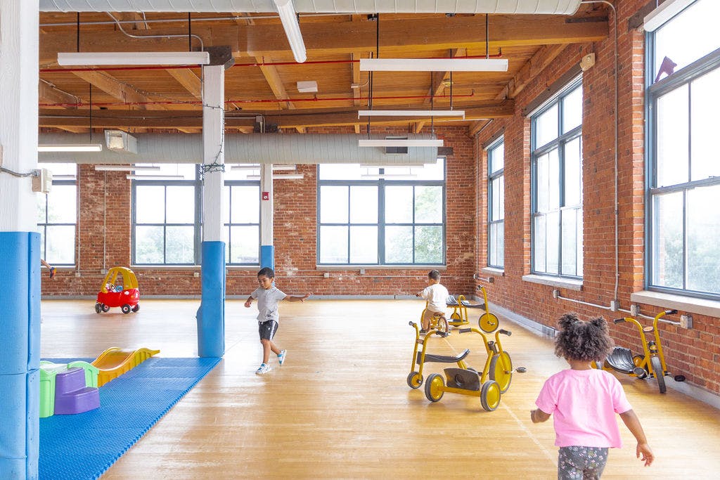 Children playing in a large room with brick walls and many windows