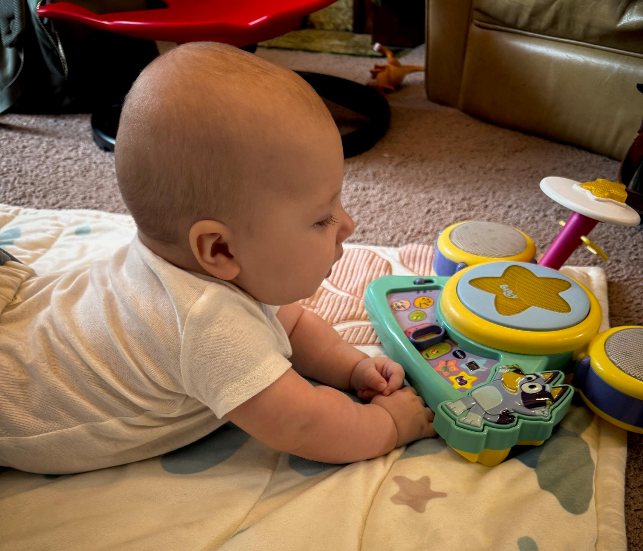 Child lying on stomach playing with a toy drum set