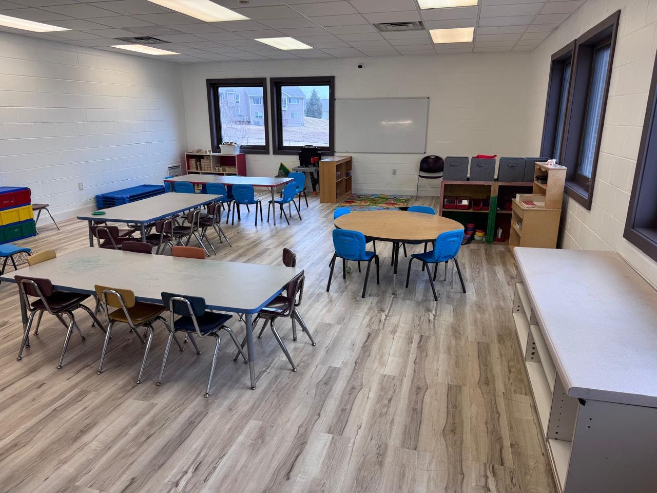 Empty classroom with multiple tables and chairs, and large windows
