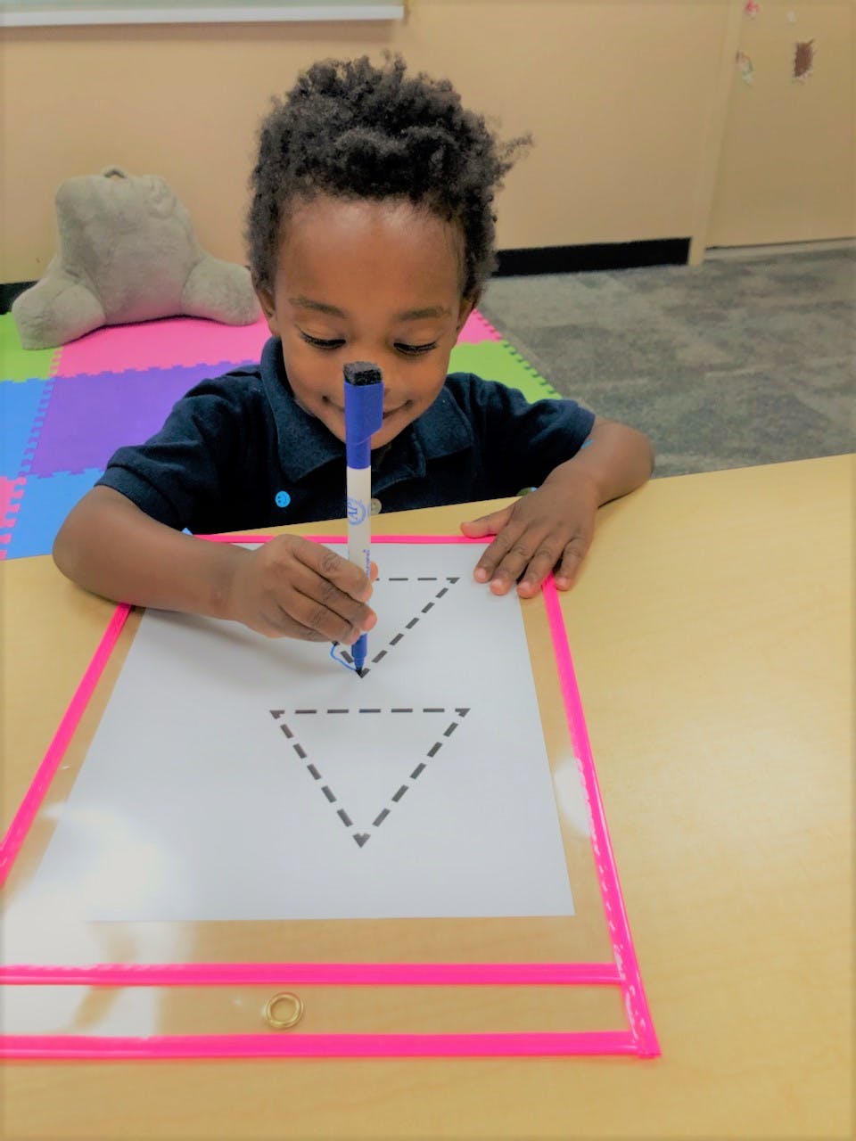 Child tracing a triangle shape on a paper with a marker