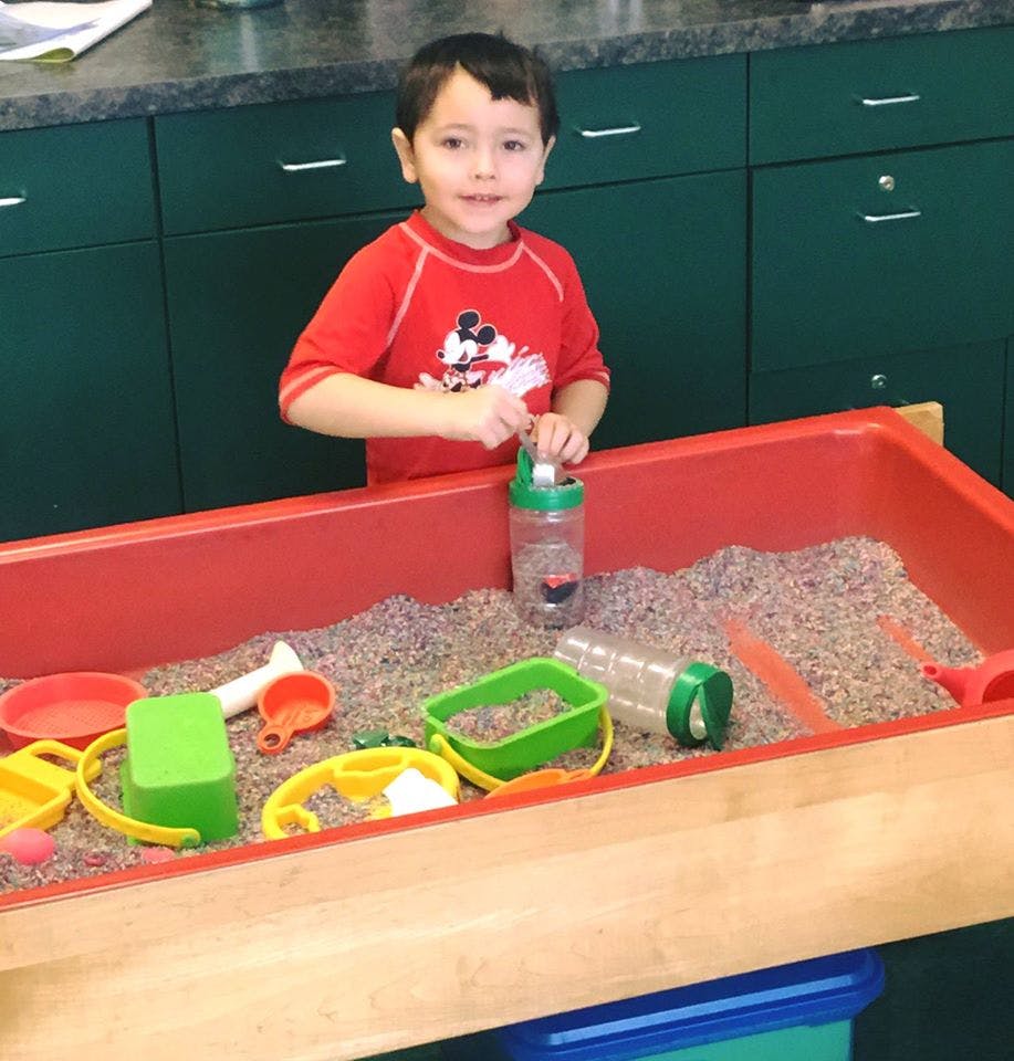 Child playing in a sand table with toys