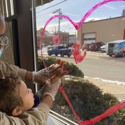 Person helping a child make red handprints on a window