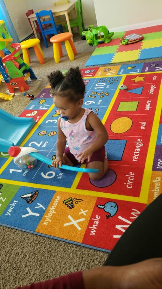 Child kneeling on a colorful alphabet rug playing with a toy