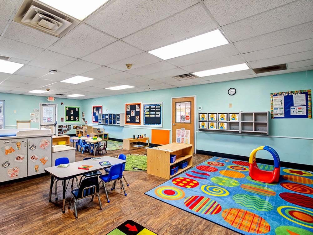 Classroom with small tables and chairs, toys, and colorful rugs
