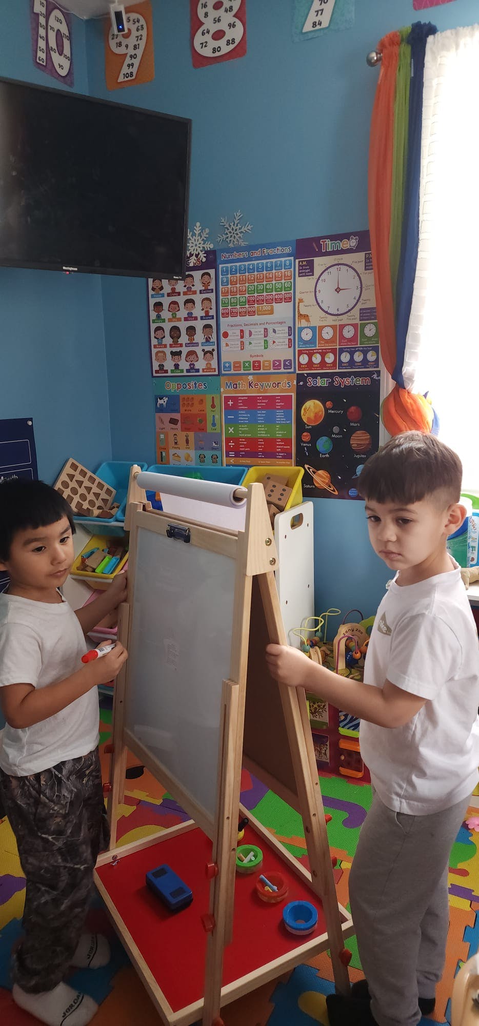 Two children standing at an easel, one holding a marker