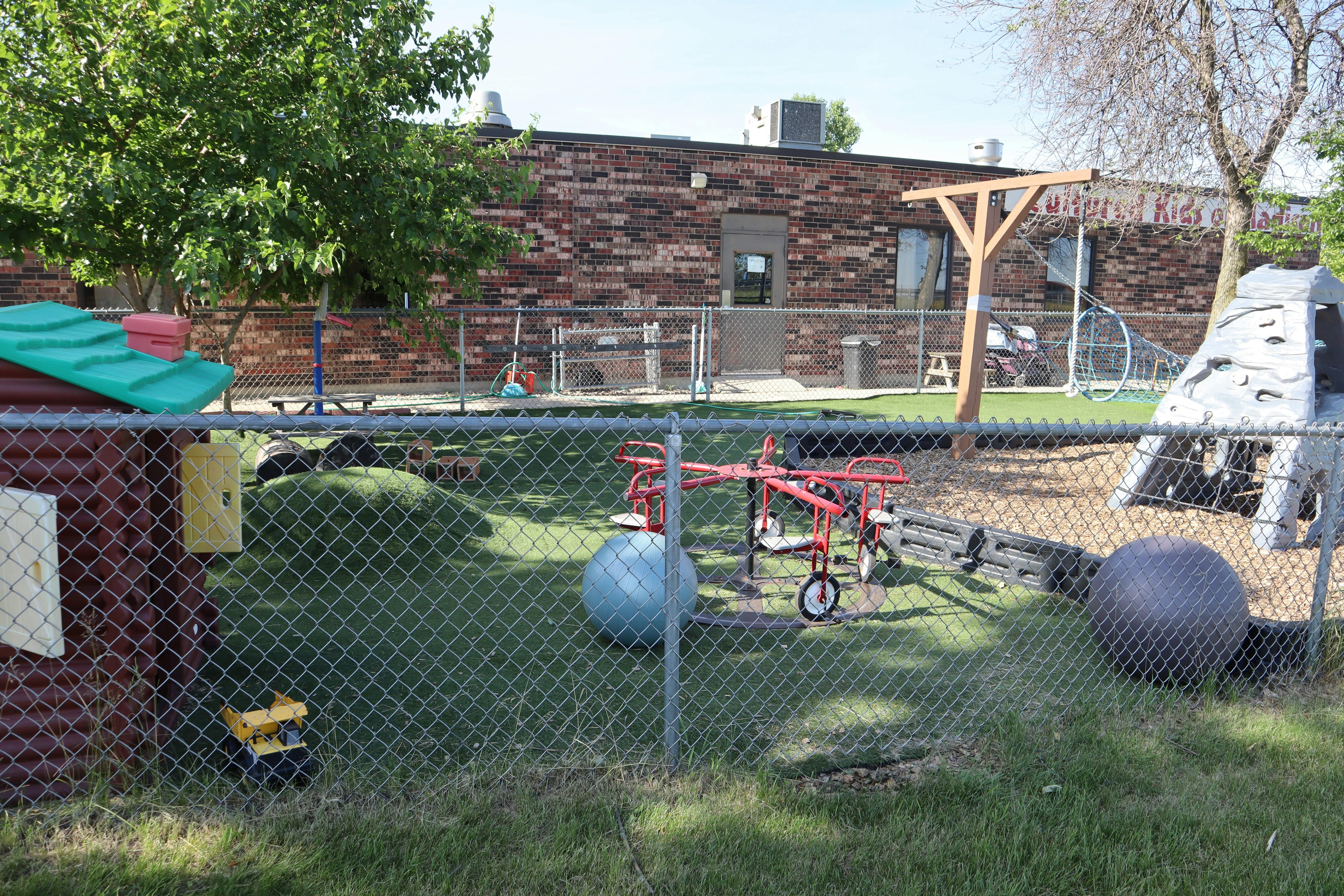 Outdoor playground with various play equipment and a brick building in the background