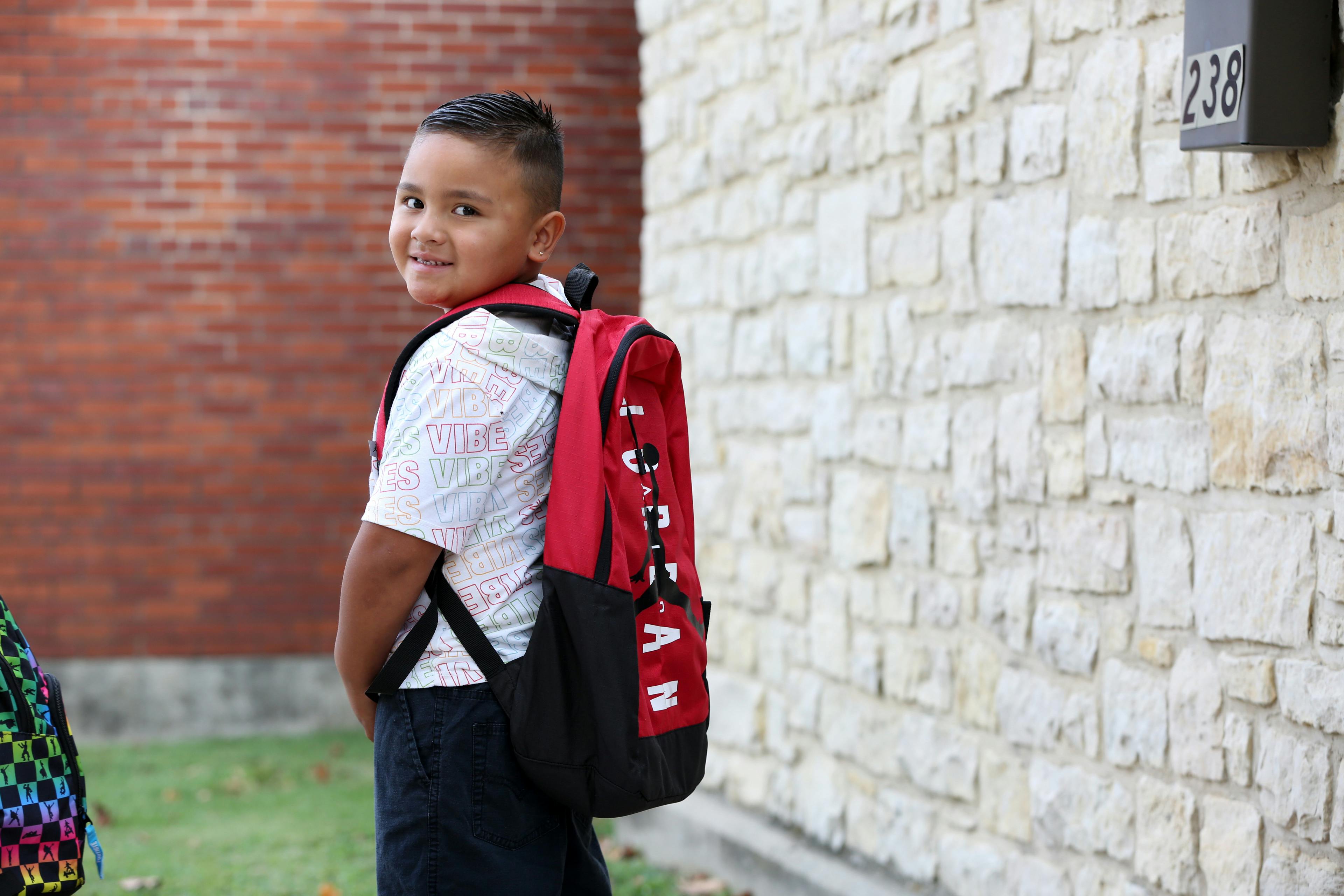Child wearing a red backpack looking over shoulder