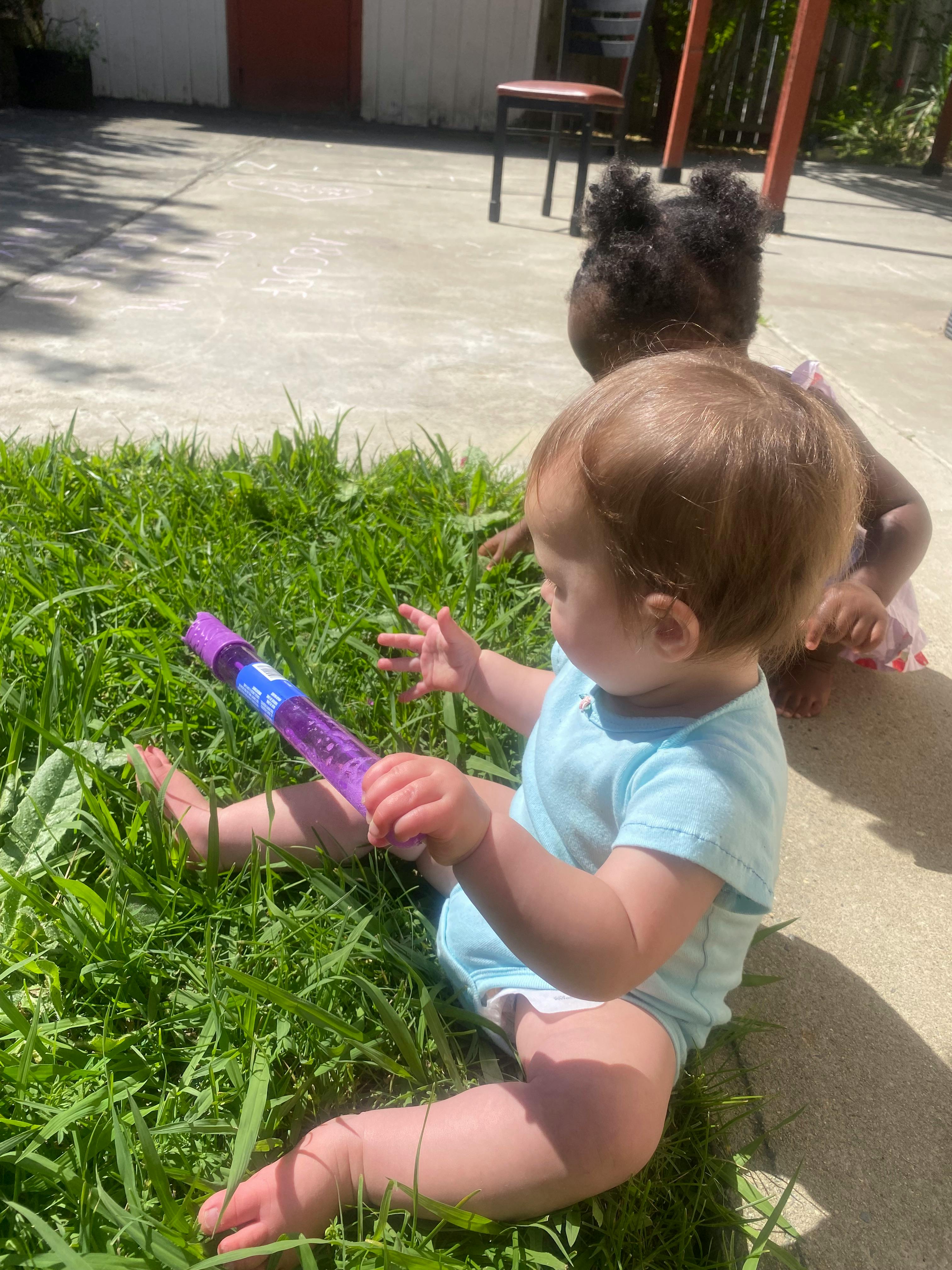 Two children playing in grass, one holding a purple bubble wand