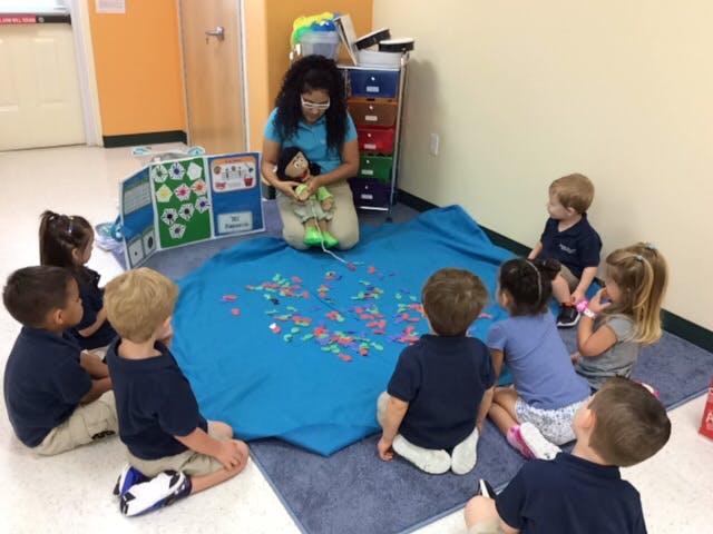 Adult and children sitting on floor around a blue mat with small objects