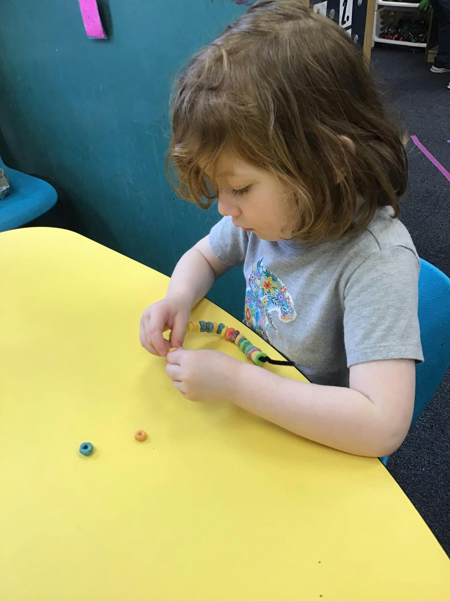 Child stringing colorful beads on a yellow table