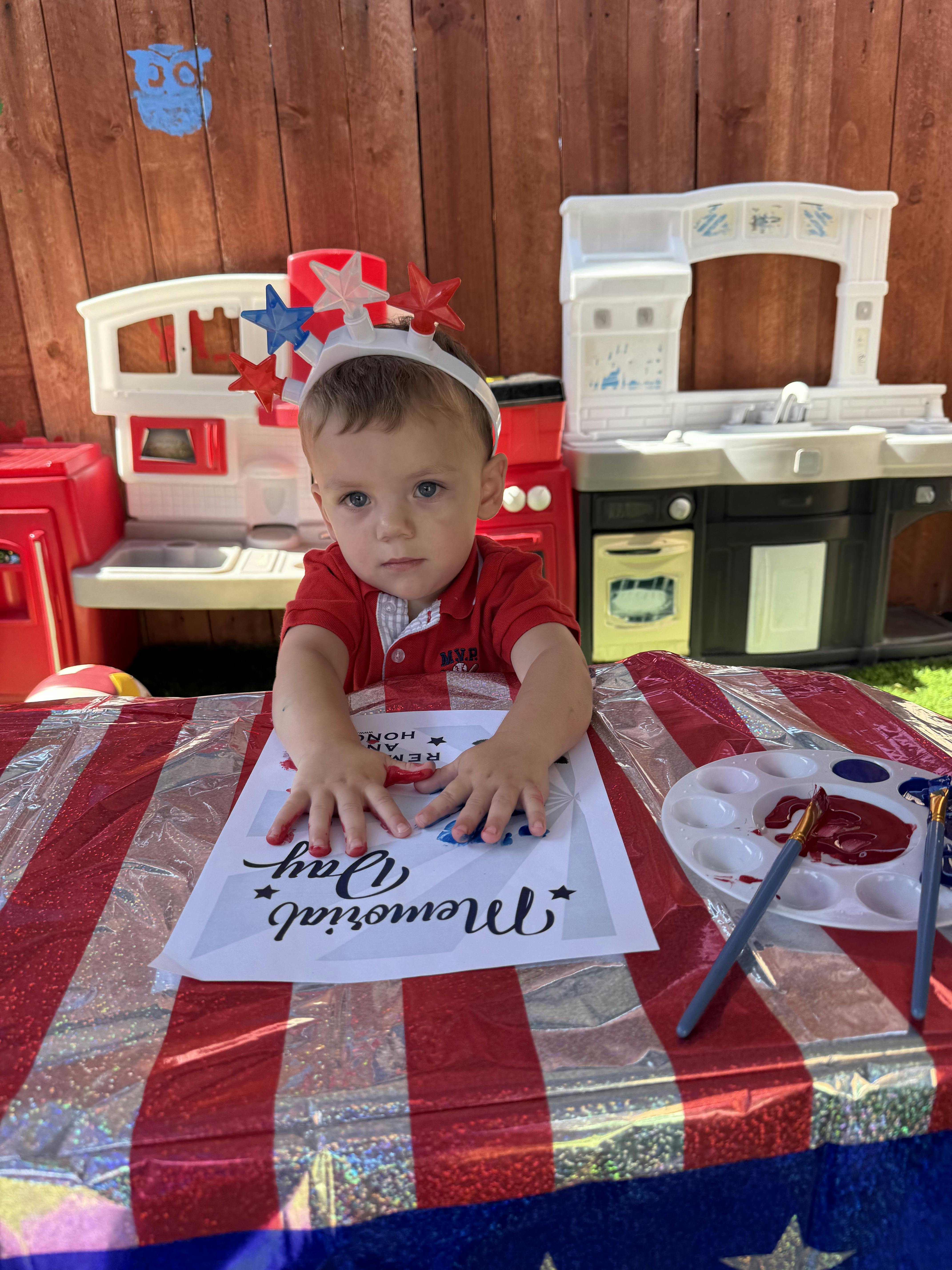 Child with red and blue paint on hands, wearing a star headband, painting