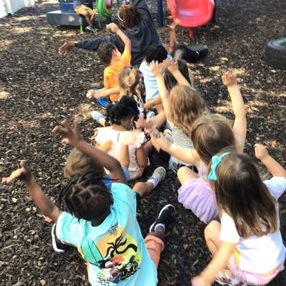 Group of children sitting on the ground with arms raised