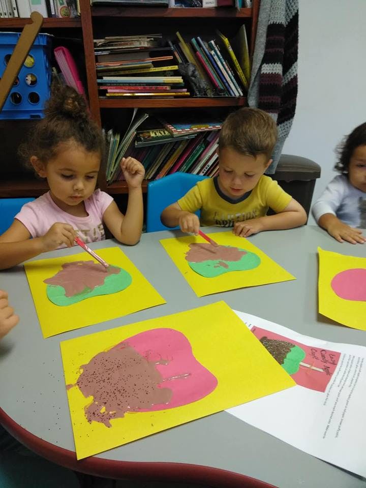 Children painting on yellow paper at a table