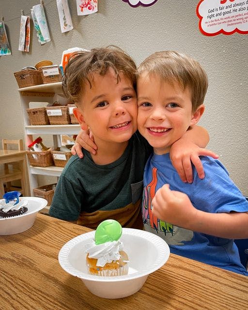 Two children smiling and hugging at a table with cupcakes