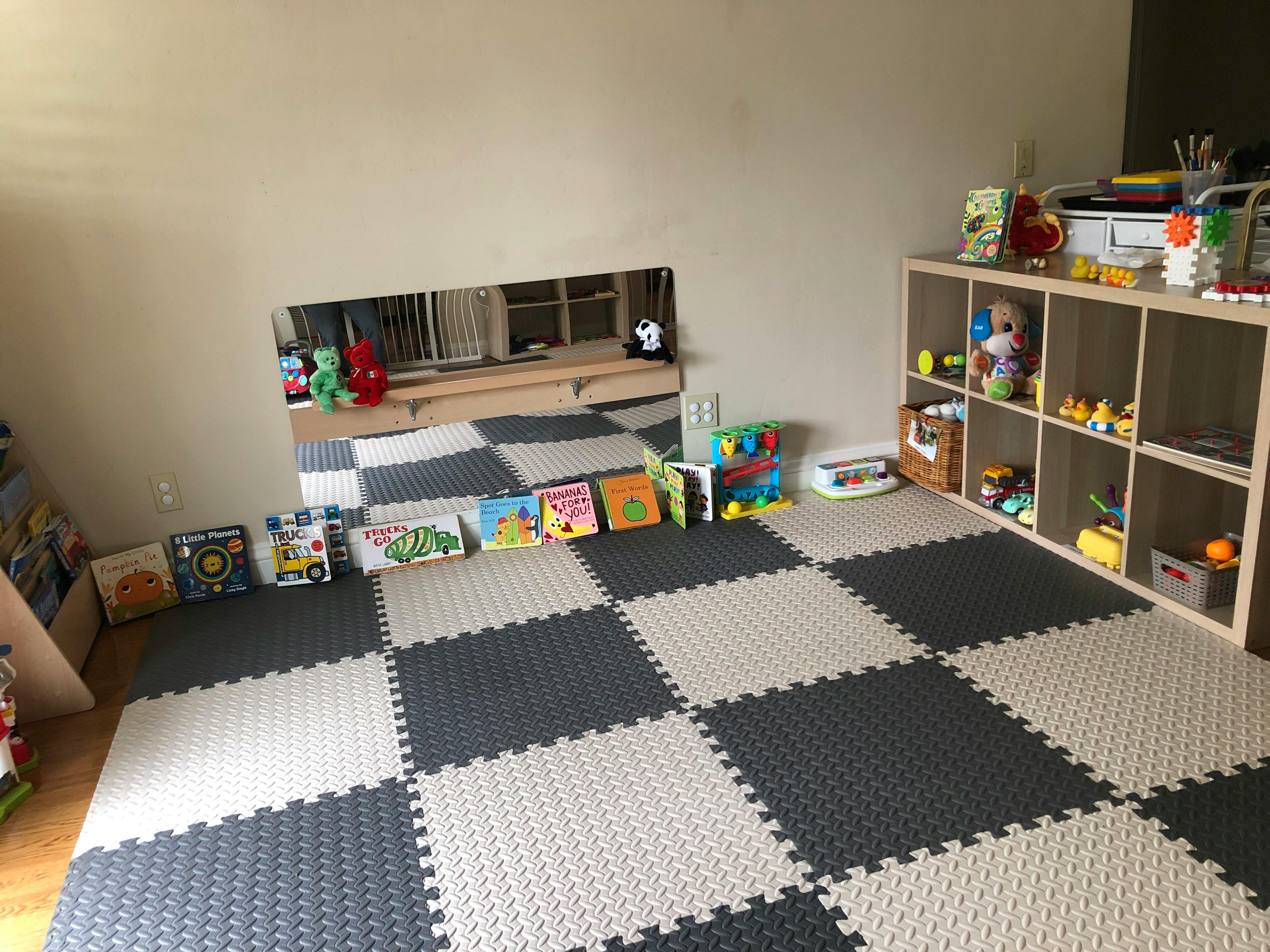Playroom with checkered floor mats, a mirror, and a shelf with toys