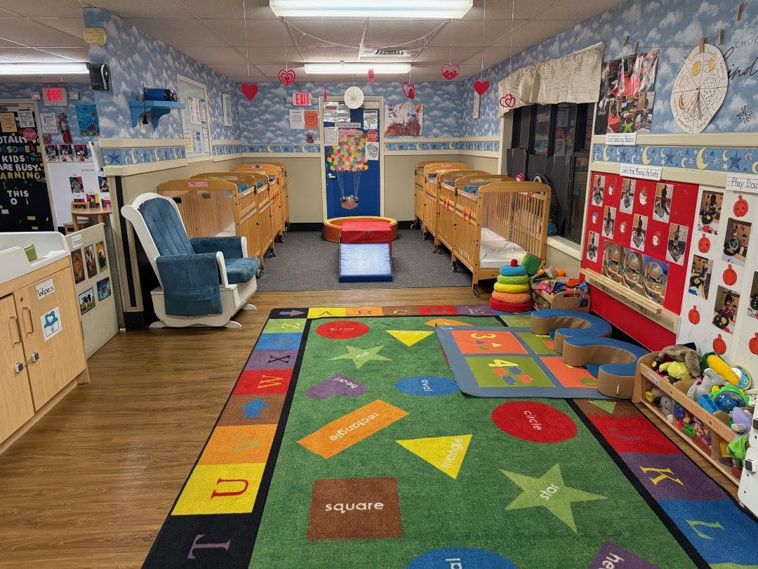 daycare classroom with multiple cribs, a rocking chair, and a playmat