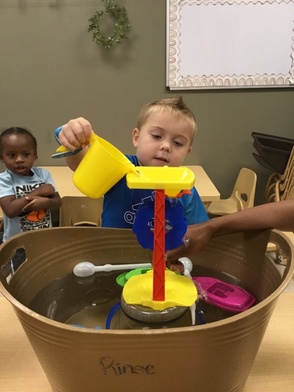 Child pouring water into a water play toy in a large tub