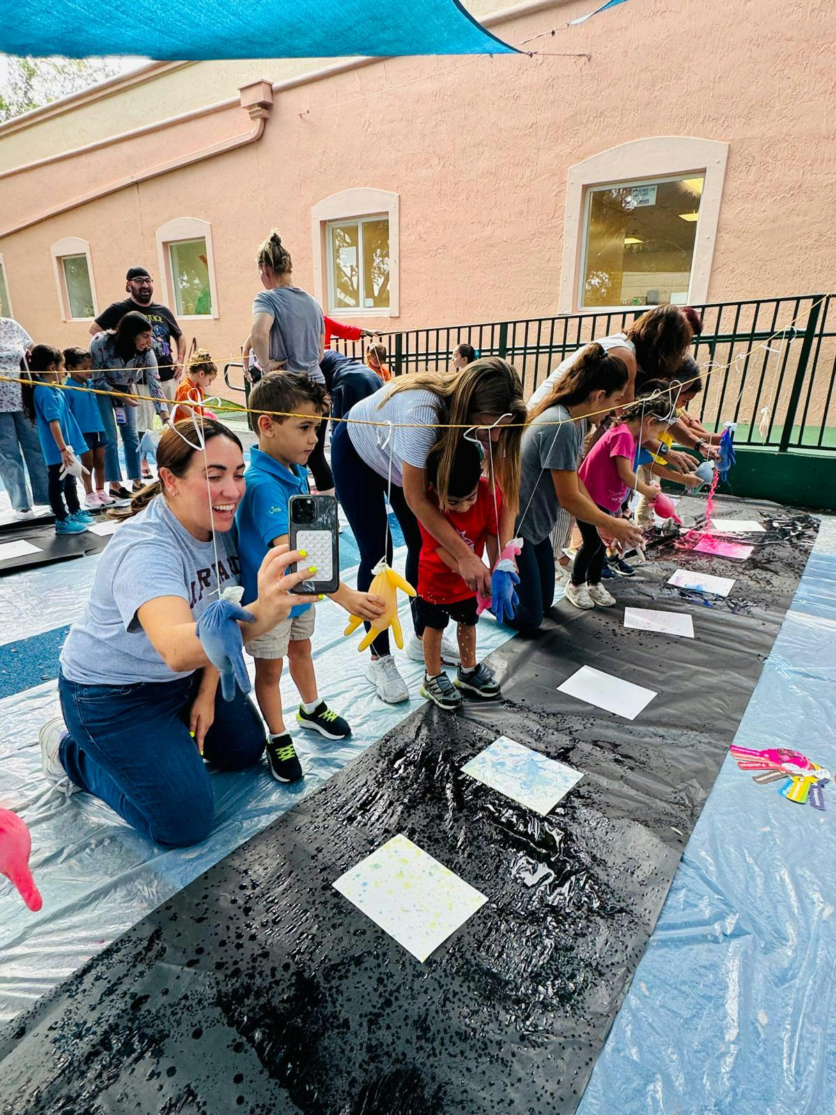 People and children painting on a long black tarp