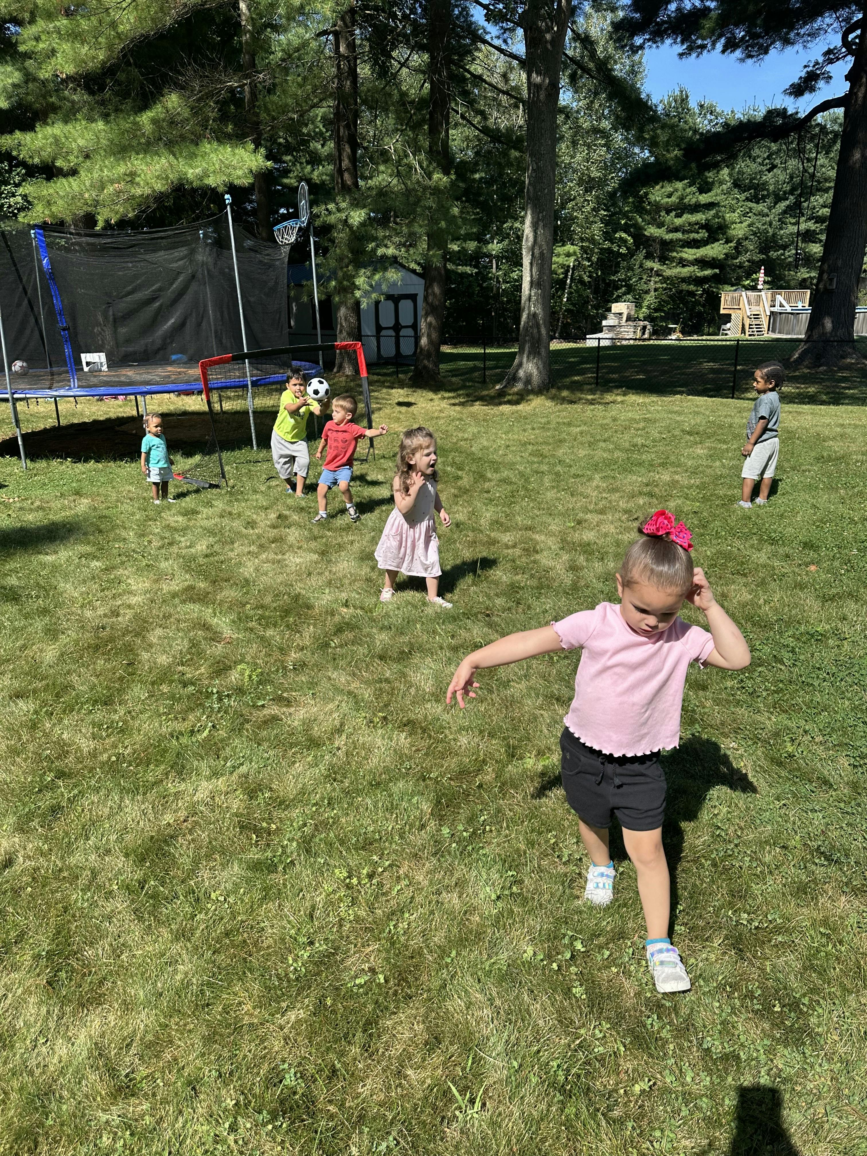 Children playing in a grassy yard with a trampoline and soccer goal