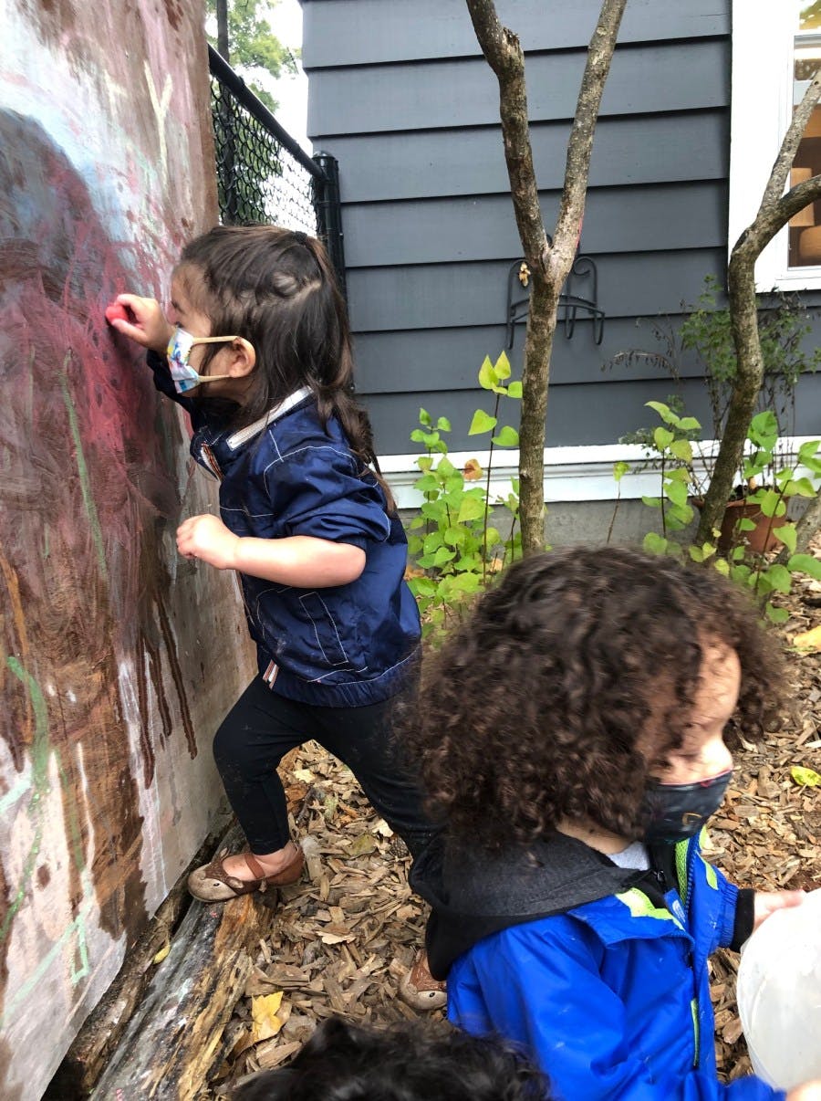 Child in a mask drawing on a wooden wall outdoors