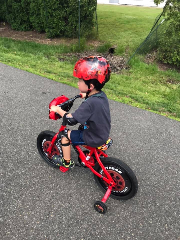 Child wearing a helmet and knee pads riding a red bicycle with training wheels