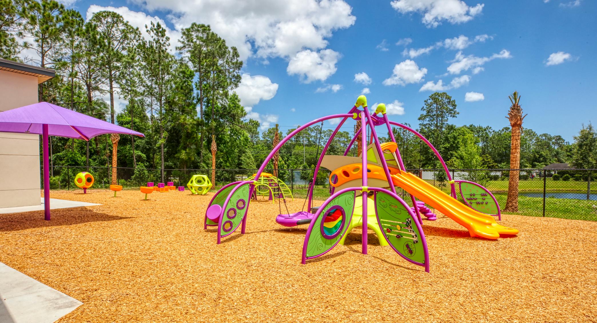 Colorful playground with various equipment on wood chips under a blue sky