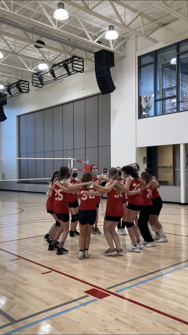 Group of athletes in red jerseys huddled on a volleyball court
